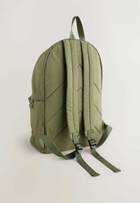 Mochila verde oliva con textura acolchada, dos correas de hombro acolchadas y un asa superior. Cuenta con un bolsillo lateral y correas ajustables con hebillas.