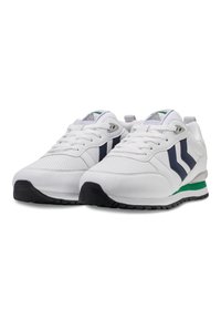 Un paio di scarpe da ginnastica bianche con strisce laterali blu navy, accento verde sulla suola intermedia, suole nere e lacci bianchi su uno sfondo bianco.