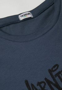 Námořnická modrá bavlněná tričko s kulatým výstřihem a krátkými rukávy. Na přední straně jsou vytištěný černý text v tučném stylu připomínajícím štětcový tah.