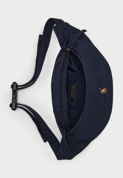 Marinefarbener Canvas Bauchtasche mit einem Reißverschluss, ausgestattet mit einem Logoschild und einem gestickten Emblem. Verstellbare Riemen und robuste Beschläge.