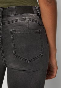 Svarte denimjeans har en tettsittende design med en glatt tekstur, baklomme og en lærdeltaske.