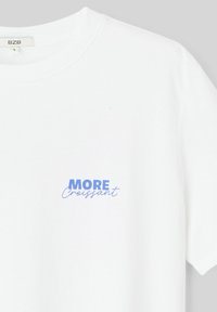 T-shirt en coton blanc avec un col rond. Le texte imprimé indique "MORE Croissant" en bleu. Design simple et classique avec des manches courtes.