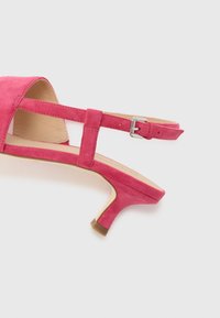 Rosa semsket høyhælte sko med en tynn ankelstropp og rund tå. Hælen er omtrent 5 cm høy og har en kontrasterende brun såle.