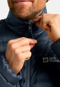 Doudoune navy avec un col haut, finition texturée et fermeture éclair contrastante. Comprend le logo de la marque sur la poitrine.