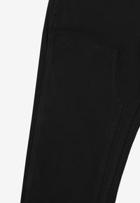 Czarne spodnie o gładkiej fakturze i bocznej kieszeni. Projekt z prostym krojem i minimalnymi detalami szycia, skoncentrowany na funkcjonalności.