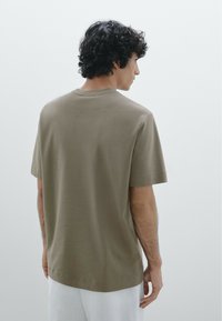 T-shirt a maniche corte, dalla vestibilità rilassata, in cotone verde oliva. Caratterizzato da un collo rotondo e una texture liscia. Design semplice e minimalista.