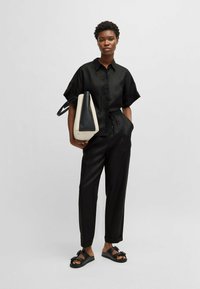 Czarna koszula z krótkim rękawem, zestawiona z czarnymi zwężającymi się spodniami. Trzyma czarną i kremową torebkę, nosi czarne sandały z akcentami.