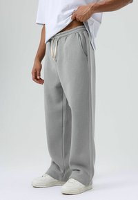 Pantalon de survêtement gris clair en tissu doux, avec une taille élastique munie d'un cordon de serrage, des poches latérales et une coupe décontractée.