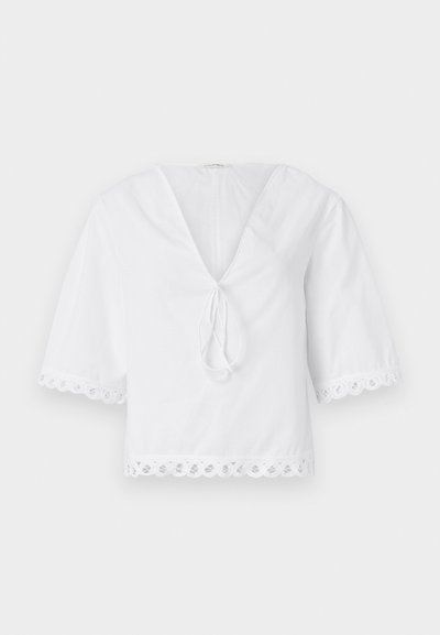 Fehér pamut blúz V-nyakkal, elöl masni részlettel és csipkebetétes, fodros ujjak és hem. Rövid puffos ujjakkal.
