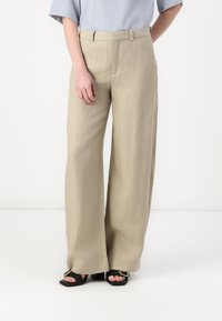 Beige linbukser med rett kutt-design, med middels høy midje, sidelommer og en glatt tekstur. Kombinert med svarte hælsandaler.