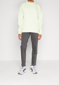 Lichtgroene sweatshirt met lange mouwen en ronde halslijn, gecombineerd met donkergrijze broek en witte sneakers met zwarte en rode accenten.