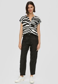 Zwart-witte zebra print shirt met een V-hals en korte mouwen, gecombineerd met zwarte broek met cargozakken en witte sneakers.