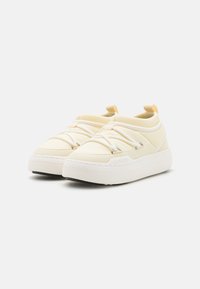Sneakers in tela gialla chiara con lacci elastici, suola in gomma, forma arrotondata e design minimalista. Presentano il logo sul lato.