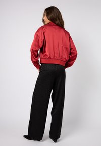Czerwona satynowa kurtka bomberka z elastycznym dołem, zestawiona z czarnymi szerokimi spodniami z subtelnym wzorem w panterkę i gładką fakturą.