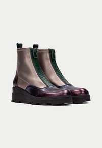 Botas de tobillo metálicas con una suela negra gruesa, que presentan un acabado en bronce y púrpura profundo, acentos de cremallera verde y una parte superior de textil suave.