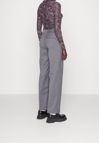 Genomskinlig långärmad topp i mörklila med blommönster, kombinerad med högmidjade grå vida byxor och klumpiga svarta skor.