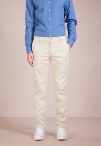 Ljust beige chinos med rak passform, med framfickor, knäppning med knapp, och bärs med vita sneakers. Blå skjorta med prickar ovanför.