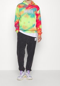 Bunte Batik-Hoodie in Grün, Pink und Blau mit Kängurutasche; kombiniert mit schwarzen schmal geschnittenen Jogginghosen und grauen Sneakers mit Akzenten.
