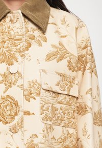 Ziedu raksta beidzēta auduma jaka ar strukturētu brūnu korduroja apkakli, ar pogu aizdari un kabatu ar atloku.