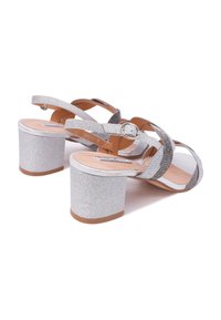 Sandali con tacco a blocco argentato e cinturini luccicanti, dotati di chiusura con fibbia e solette beige lisce. Gli accenti testurizzati sui cinturini aggiungono un tocco di dettaglio.