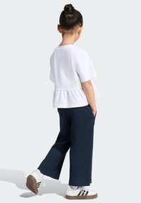 Top blanco de algodón de manga corta con bajo peplum, combinado con pantalones anchos de canalé en azul marino y zapatillas blancas con rayas negras.