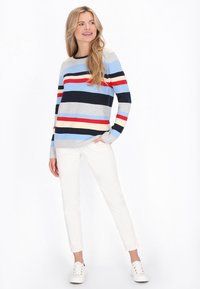 Stripet sweater i blå, navy, grå, rød og creme; med lange ærmer; rund hals; kombineret med hvide bukser og hvide sneakers.