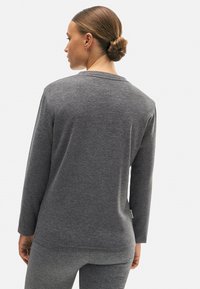 Camisa de manga larga gris en un tejido suave con un corte holgado, que presenta un escote redondeado y detalles cosidos en el dobladillo.