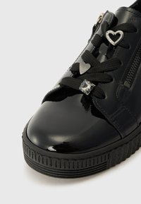 Baskets noires en vernis avec des lacets noirs texturés, des embellissements en forme de cœur et de carré, et une semelle en caoutchouc à zigzag. Fermeture éclair sur le côté.