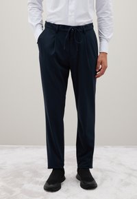 Marineblaue, lässige Hose mit elastischem Bund, Kordelzug und seitlichen Taschen. Das Material wirkt glatt und leicht.