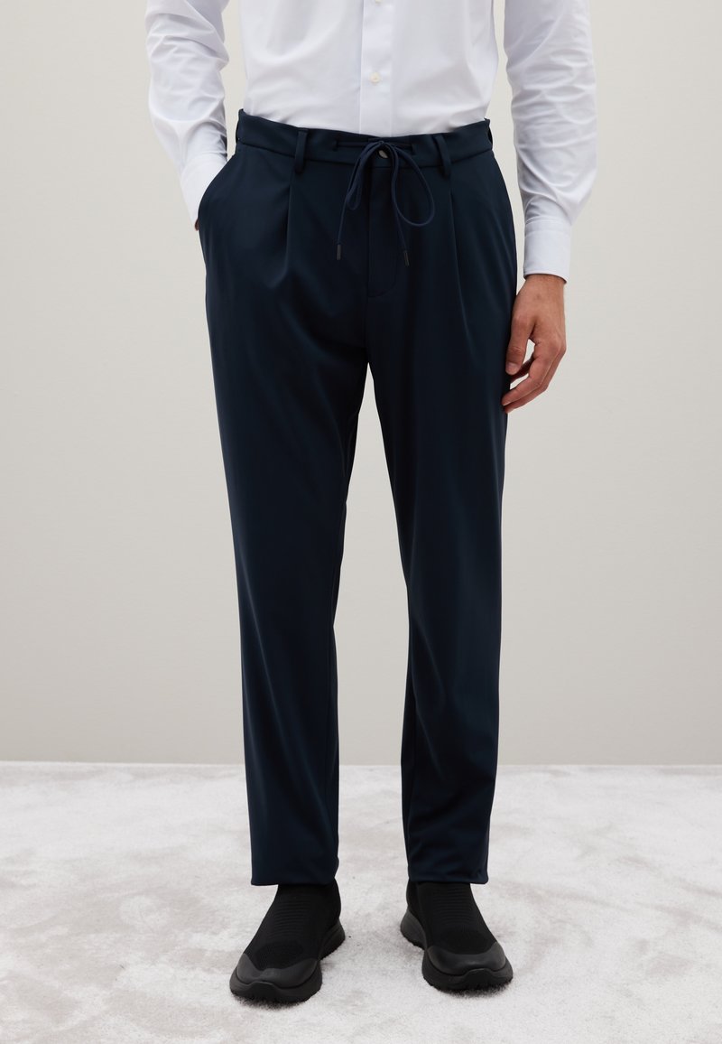 Marineblaue, lässige Hose mit elastischem Bund, Kordelzug und seitlichen Taschen. Das Material wirkt glatt und leicht.