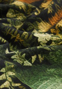 Textil mit dunklem Hintergrund und grünen sowie gelben botanischen Mustern. Die Stoffstruktur wirkt weich und leicht zerknittert.