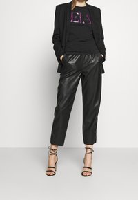 Svart kavaj i kombination med en svart t-shirt med rosa paljettskrift, och svarta fusk-lädercroppade byxor. Svarta högklackade sandaler med remmar.