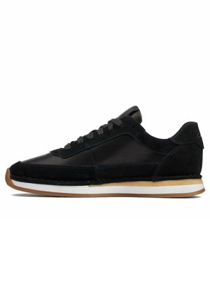 Black low-top sneaker with suede and leather panels, black laces, white midsole, and brown rubber outsole, shown in side profile.