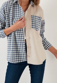 Camicia a quadri con un lato in motivo gingham blu e bianco e l'altro in tessuto beige, dotata di una singola tasca sul petto e chiusura con bottoni.