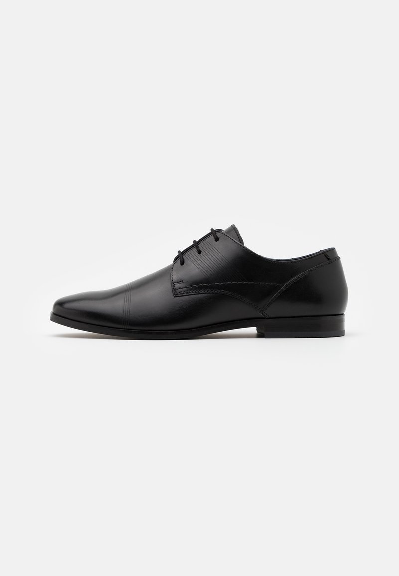 Chaussure habillée en cuir noir avec un bout pointu, un laçage, et de subtils accents texturés sur le dessus. Talon plat et profil minimaliste.