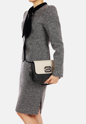 Abito grigio con texture e colletto in velluto nero; tiene una borsa a spalla nera e crema con una fibbia a catena.