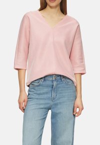 Rosa- und weißgestreiftes Oberteil mit V-Ausschnitt, Dreiviertelärmeln und lässiger Passform, kombiniert mit hellblauen geraden Jeans.