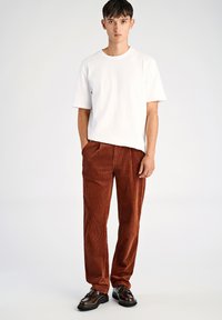 Hvid bomuld t-shirt, løs pasform, kombineret med rustfarvede kordsfløjlsbukser med lodrette striber. Modellen har sorte lædersko på.