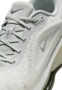 Šviesiai pilki sportiniai batai su tekstūruota viršutine dalimi, tinklinėmis detalėmis ir sidabriniu Nike logotipu. Ypatybės: sustiprintas kulnas ir paminkštintas padas.