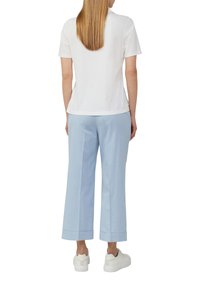 Weißes Baumwoll-T-Shirt kombiniert mit hellblauen, weit geschnittenen Hosen mit umgeschlagenen Säumen und weißen Turnschuhen. Schlichtes, entspanntes Outfit-Design.