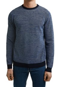 Granatowy sweter dzianinowy o wzorzystym wykończeniu, okrągłym dekolcie oraz kontrastowych ściągaczach w mankietach i u dołu. Noszony z niebieskimi dżinsami.