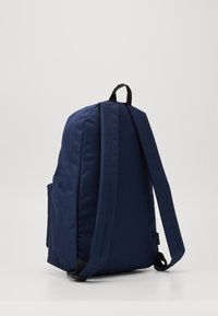 Zaino blu navy con spallacci imbottiti, tasca laterale e maniglia superiore. Realizzato in tessuto resistente con una texture liscia.