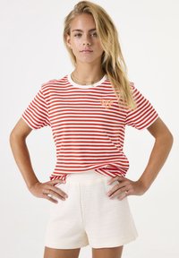 Camiseta de rayas rojas y blancas con cuello redondo y mangas cortas, combinada con pantalones cortos blancos texturizados. Presenta un pequeño logo en el pecho.