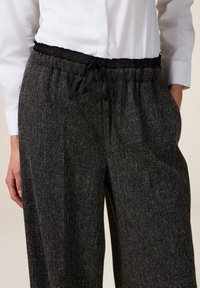Grijze textuurbroek met een zwarte elastische tailleband en koord. Heeft zijzakken en een losse pasvorm, geschikt voor casual wear.