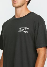 T-shirt en coton noir à manches courtes, arborant un logo Volcom blanc sur le côté gauche de la poitrine. Texture douce, coupe standard.