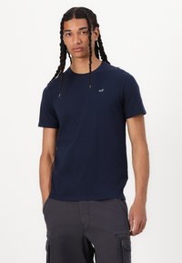 Marineblaue Baumwoll-T-Shirt mit kurzen Ärmeln und Rundhalsausschnitt. Kleines Logo auf der Brust. Glatte Textur, lässiger Schnitt, minimalistisches Design.