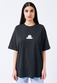 Černé oversize tričko vyrobené z bavlny, které má na hrudníku světle modrý grafický design znázorňující název značky.