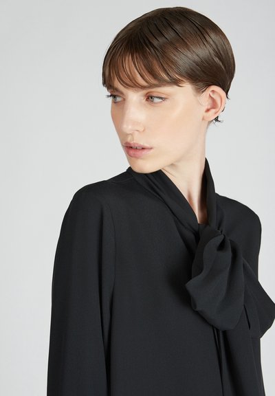 Blusa nera con collo alto e un grande dettaglio a fiocco, con maniche lunghe, realizzata in tessuto leggero e testurizzato.
