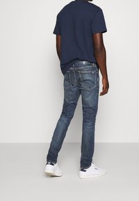 Mörkblå bomulls-T-shirt med korta ärmar, kombinerad med åtsittande ljusblå jeans. Vita sneakers fulländar den avslappnade stilen.