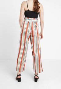 Femme portant un pantalon taille haute à jambes larges avec des rayures verticales multicolores et un haut noir sans manches, vue de dos.